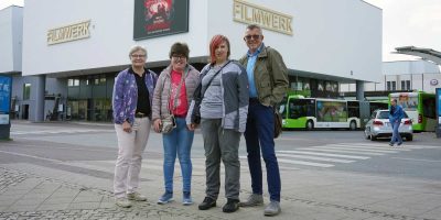 Zwei Menschen mit Behinderung und zwei ehrenamtliche Betreuer posieren vor einem Kino während eines gemeinsamen Kinobesuchs.